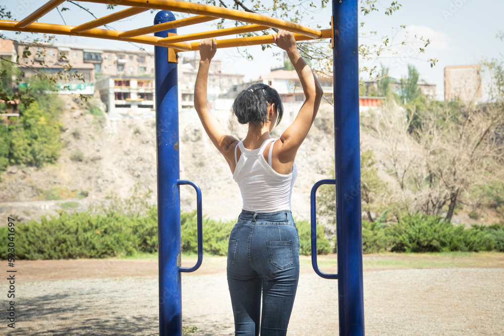 Obraz premium Girl climbing and hanging on outdoor horizontal bar.