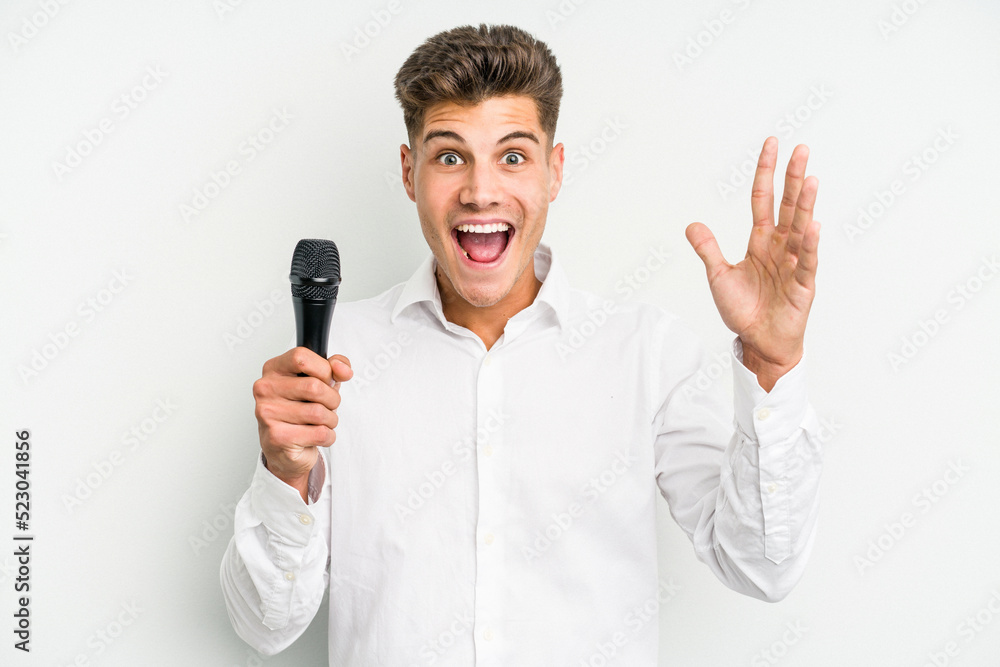 Young singer caucasian man isolated on white background receiving a pleasant surprise, excited and raising hands. Young singer caucasian man isolated on white background receiving a pleasant surprise, excited and raising hands.