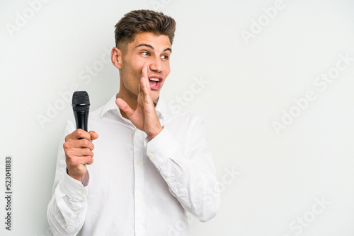 Young singer caucasian man isolated on white background is saying a secret hot braking news and looking aside