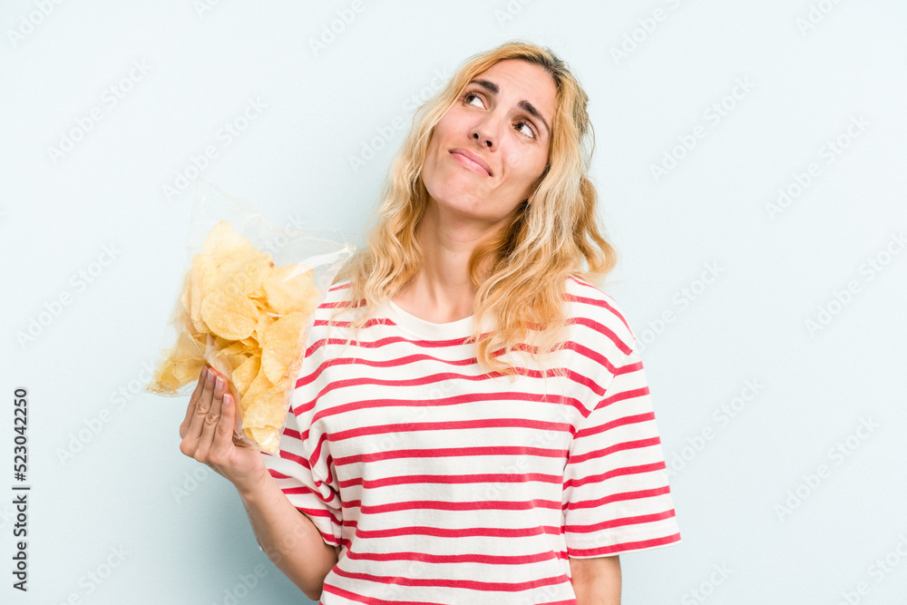 Young caucasian woman holding a bag of chips isolated on blue background dreaming of achieving goals and purposes Young caucasian woman holding a bag of chips isolated on blue background dreaming of achieving goals and purposes