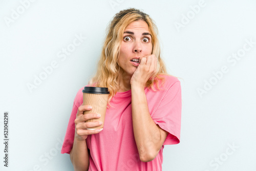 Young caucasian woman holding a take away coffee isolated on blue background biting fingernails, nervous and very anxious.