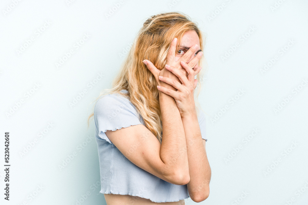 Young caucasian woman isolated on blue background blink through fingers frightened and nervous. Young caucasian woman isolated on blue background blink through fingers frightened and nervous.