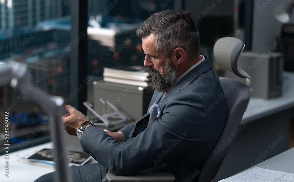 Portrait of 50s adult Caucasian businessman, CEO, boss, wearing a suit, looking out of the window of his office, business district with skyscrapers in the background Portrait of 50s adult Caucasian businessman, CEO, boss, wearing a suit, looking out of the window of his office, business district with skyscrapers in the background