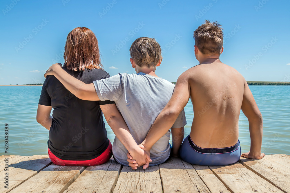 Young people sit on a wooden jetty and enjoy the magical view of the river Young people sit on a wooden jetty and enjoy the magical view of the river