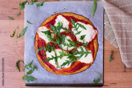 Pizza con base de coliflor con salsa de tomate, queso mozzarella fresca y rúcula. Sobre bandeja de metal y papel de horno. Vista cenital. Comida saludable y sin gluten.  photo