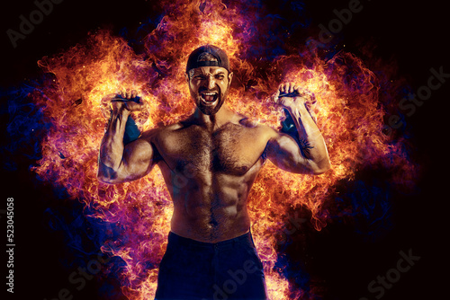 Handsome bearded shirtless tattooed bodybuilder workout wih kettlebell. Fire art concept