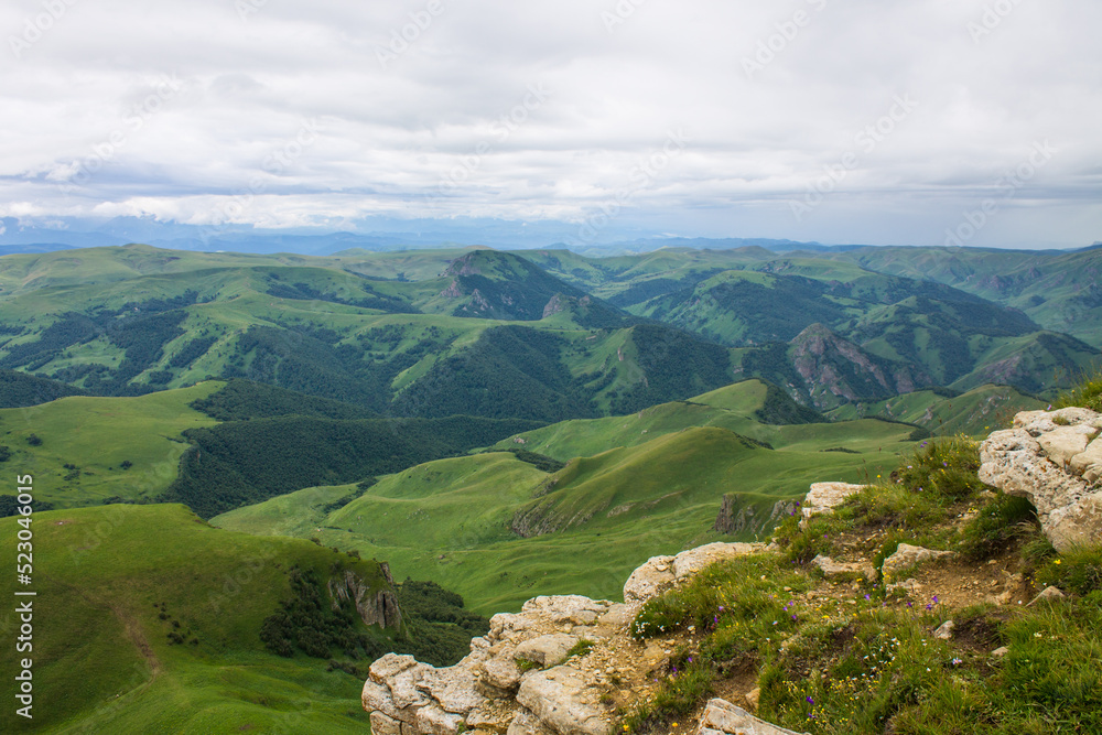 Obraz premium Beautiful landscape - panoramic view of green mountains and hills blurred in morning haze from bermamyt plateau in karachay-cherkessia Russia and dramatic clouds and copy space