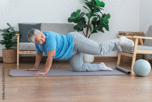 Asian elderly woman doing exercise at home by stretching the leg muscles, to people retirement age and health care concept. © Anatta_Tan