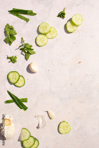 Greek tzatziki ingredients flat lay layout on white marble stone with blank space, empty copy space, cucumber, mint, garlic vertical portrait photograph