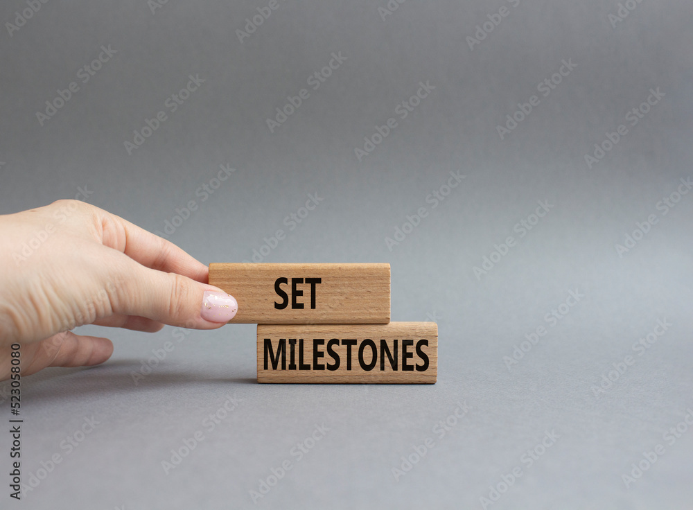 Set milestones symbol. Concept word Set milestones on wooden blocks. Beautiful grey background. Businessman hand. Business and Set milestones concept. Copy space Set milestones symbol. Concept word Set milestones on wooden blocks. Beautiful grey background. Businessman hand. Business and Set milestones concept. Copy space