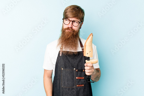 Young caucasian cobbler isolated on blue background confused, feels doubtful and unsure. photo