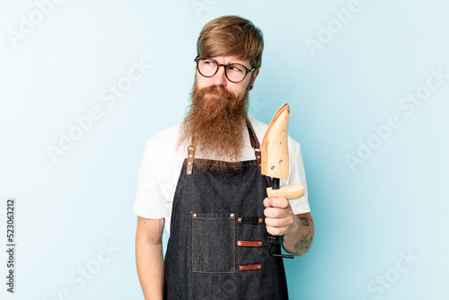 Canvastavla Young caucasian cobbler isolated on blue background confused, feels doubtful and unsure