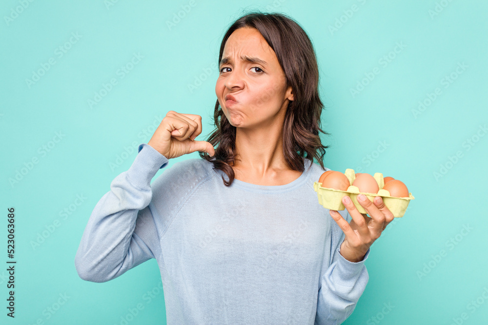 Young hispanic woman holding eggs isolated on blue background feels proud and self confident, example to follow. Young hispanic woman holding eggs isolated on blue background feels proud and self confident, example to follow.