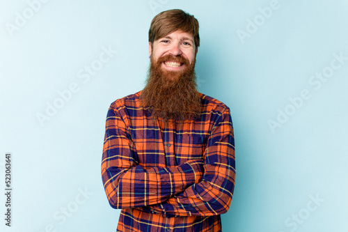 Young caucasian red-haired man isolated on blue background who feels confident, crossing arms with determination.