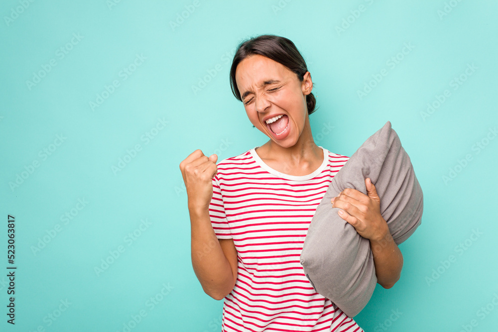 Young hispanic woman holding a cushion isolated on white background raising fist after a victory, winner concept. Young hispanic woman holding a cushion isolated on white background raising fist after a victory, winner concept.