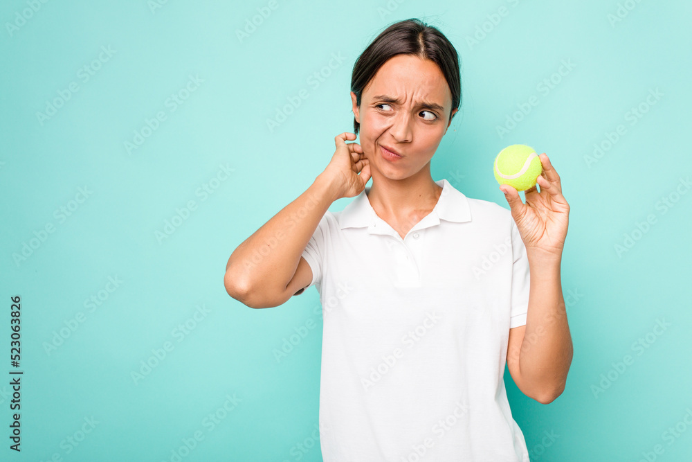 Young hispanic physiotherapy holding a tennis ball isolated on blue background touching back of head, thinking and making a choice. Young hispanic physiotherapy holding a tennis ball isolated on blue background touching back of head, thinking and making a choice.
