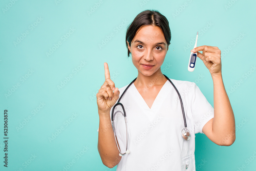 Young hispanic nurse woman holding a thermometer isolated on blue background showing number one with finger. Young hispanic nurse woman holding a thermometer isolated on blue background showing number one with finger.