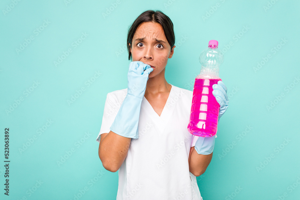 Young cleaner hispanic woman isolated on blue background biting fingernails, nervous and very anxious. Young cleaner hispanic woman isolated on blue background biting fingernails, nervous and very anxious.