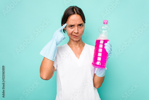 Young cleaner hispanic woman isolated on blue background pointing temple with finger, thinking, focused on a task.
