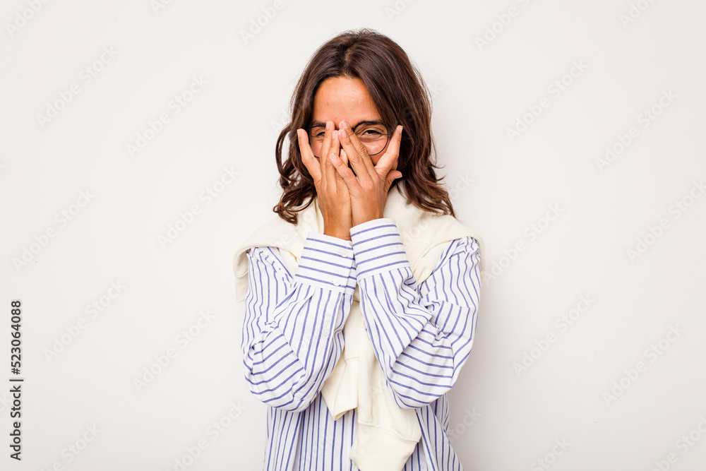 Young hispanic woman isolated on white background blink at the camera through fingers, embarrassed covering face. Young hispanic woman isolated on white background blink at the camera through fingers, embarrassed covering face.