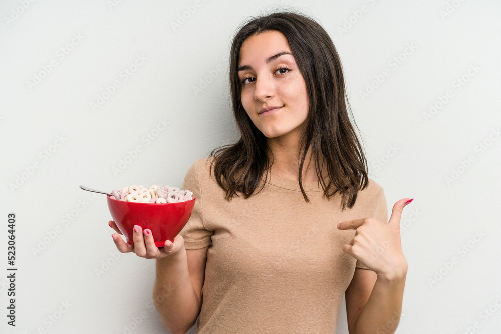 Young caucasian woman holding bowl of cereals isolated on white background person pointing by hand to a shirt copy space, proud and confident Young caucasian woman holding bowl of cereals isolated on white background person pointing by hand to a shirt copy space, proud and confident