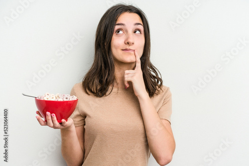 Young caucasian woman holding bowl of cereals isolated on white background relaxed thinking about something looking at a copy space.
