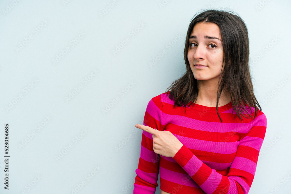 Young caucasian woman isolated on blue background smiling and pointing aside, showing something at blank space. Young caucasian woman isolated on blue background smiling and pointing aside, showing something at blank space.