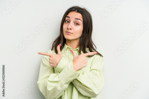 Young caucasian woman isolated on white background points sideways, is trying to choose between two options.