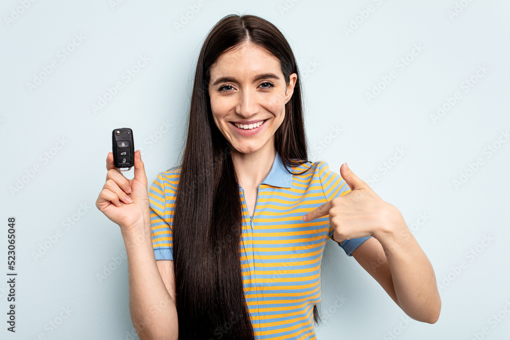 Young caucasian woman holding car keys isolated on blue background person pointing by hand to a shirt copy space, proud and confident Young caucasian woman holding car keys isolated on blue background person pointing by hand to a shirt copy space, proud and confident