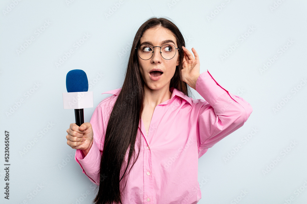 Young caucasian tv presenter woman isolated on blue background trying to listening a gossip. Young caucasian tv presenter woman isolated on blue background trying to listening a gossip.