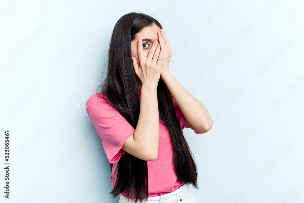 Young caucasian woman isolated on blue background blink through fingers frightened and nervous. Young caucasian woman isolated on blue background blink through fingers frightened and nervous.