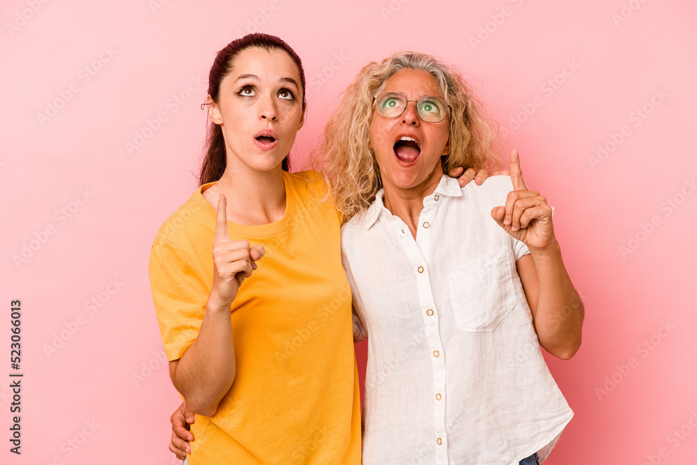 Caucasian mom and daughter isolated on pink background pointing upside with opened mouth. Caucasian mom and daughter isolated on pink background pointing upside with opened mouth.