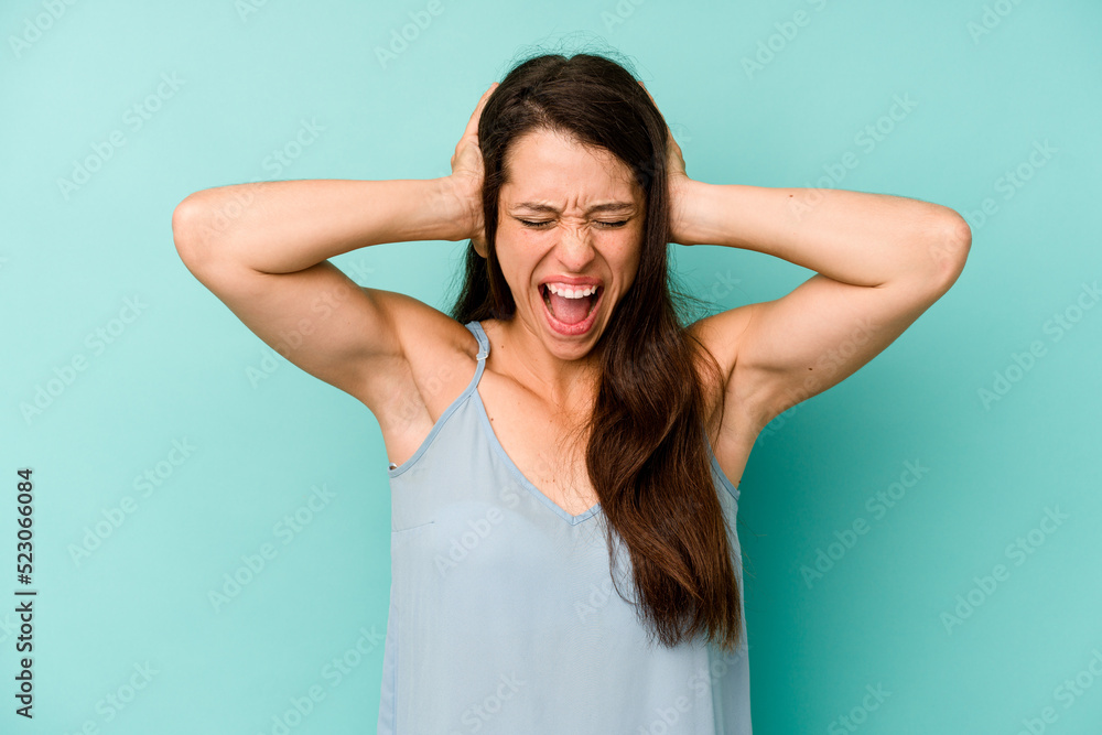 Young caucasian woman isolated on blue background covering ears with hands trying not to hear too loud sound. Young caucasian woman isolated on blue background covering ears with hands trying not to hear too loud sound.