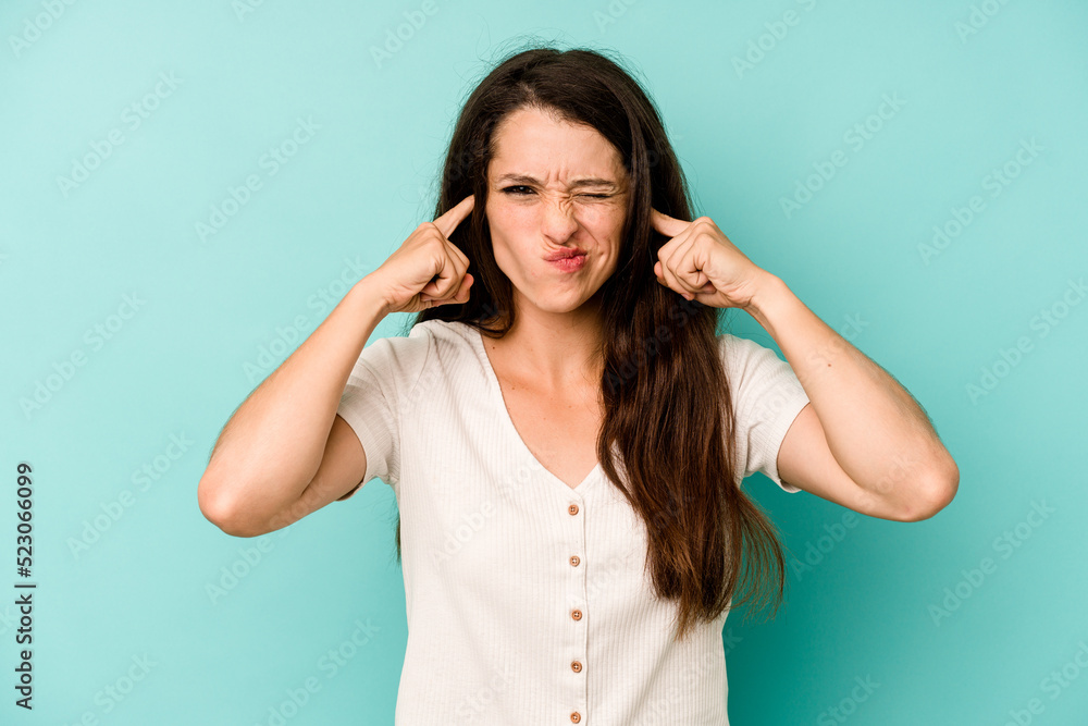 Young caucasian woman isolated on blue background covering ears with fingers, stressed and desperate by a loudly ambient. Young caucasian woman isolated on blue background covering ears with fingers, stressed and desperate by a loudly ambient.