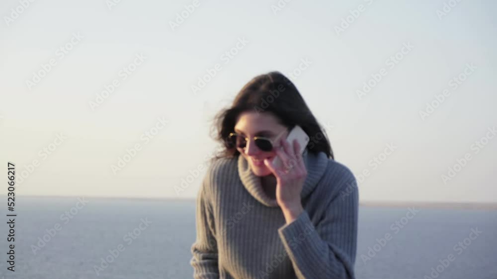 Happy beautiful woman in sweater talks on phone outdoors near sea Happy beautiful woman in sweater talks on phone outdoors near sea