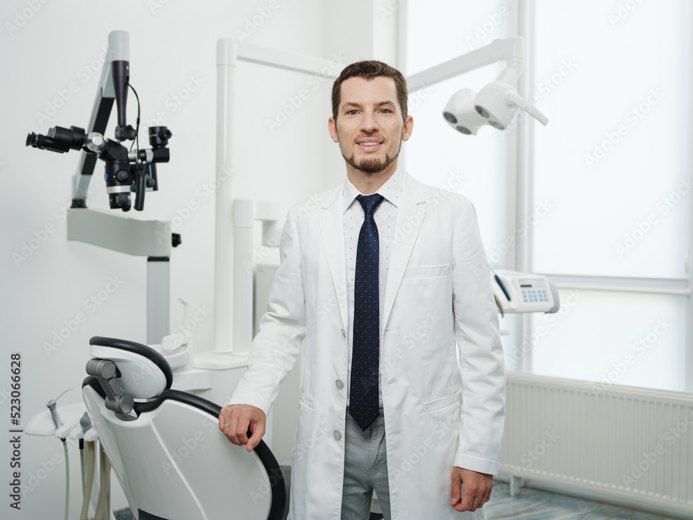 Portrait of happy male dentist wearing lab coat in white dental clinic