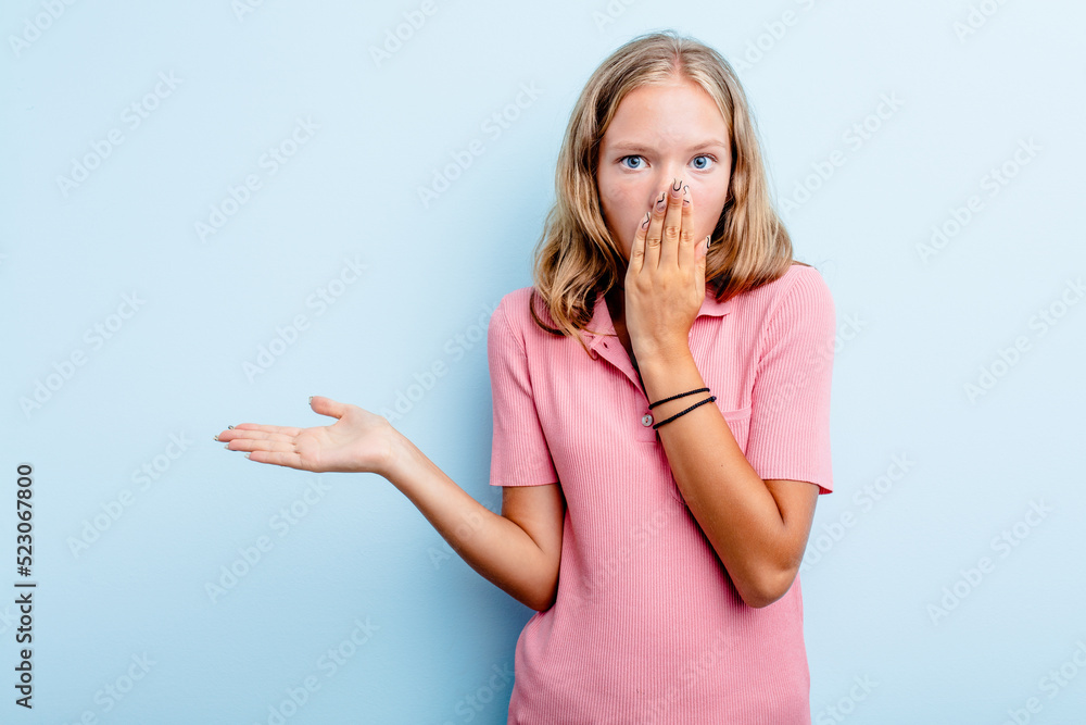 Caucasian teen girl isolated on blue background impressed holding copy space on palm. Caucasian teen girl isolated on blue background impressed holding copy space on palm.