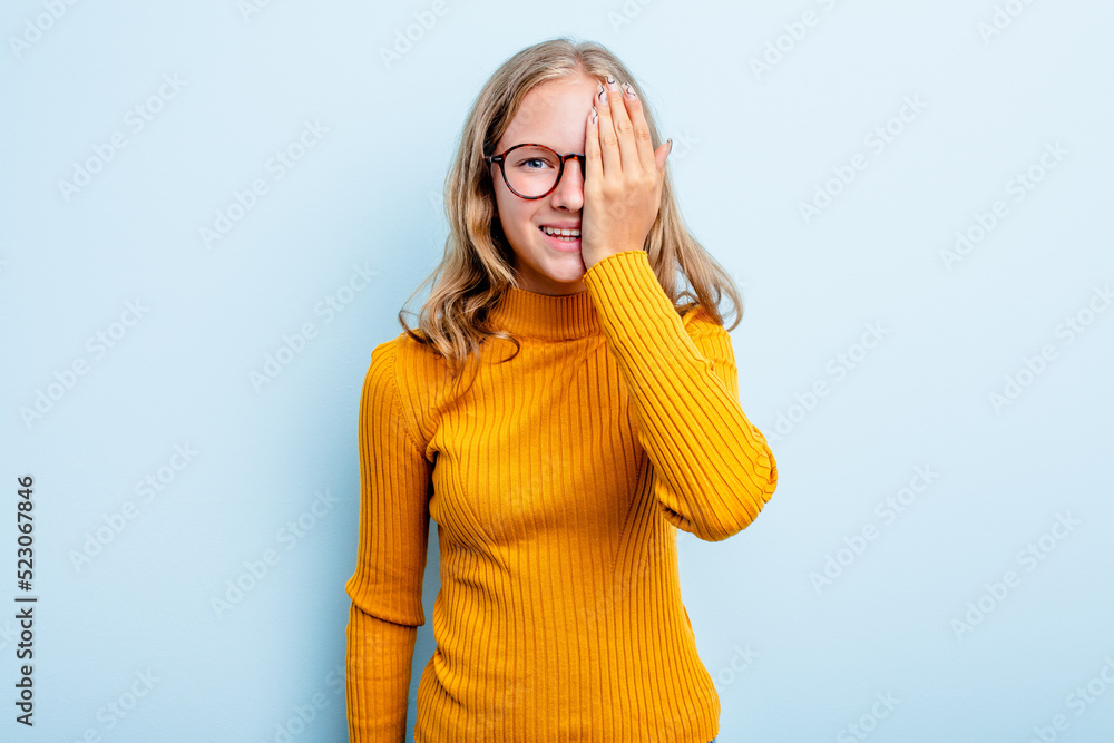 Caucasian teen girl isolated on blue background having fun covering half of face with palm. Caucasian teen girl isolated on blue background having fun covering half of face with palm.