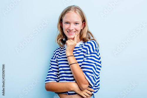 Caucasian teen girl isolated on blue background smiling happy and confident, touching chin with hand.