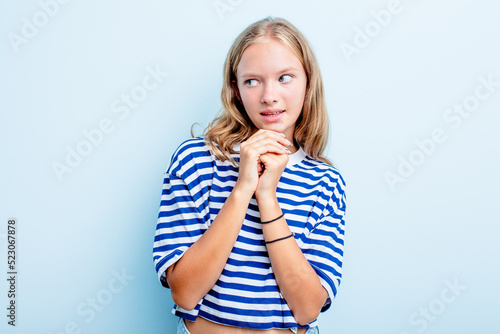 Caucasian teen girl isolated on blue background praying for luck, amazed and opening mouth looking to front.