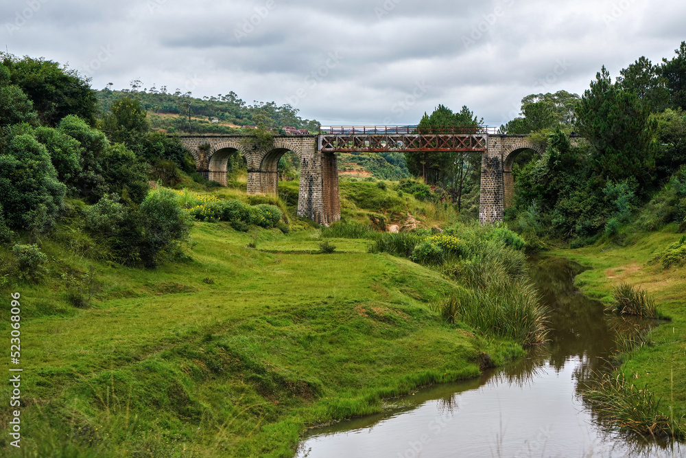 Obraz premium Small railway bridge over small river near Manjakandriana, Madagascar, green grass and trees around. There is only small number of railroads on whole island