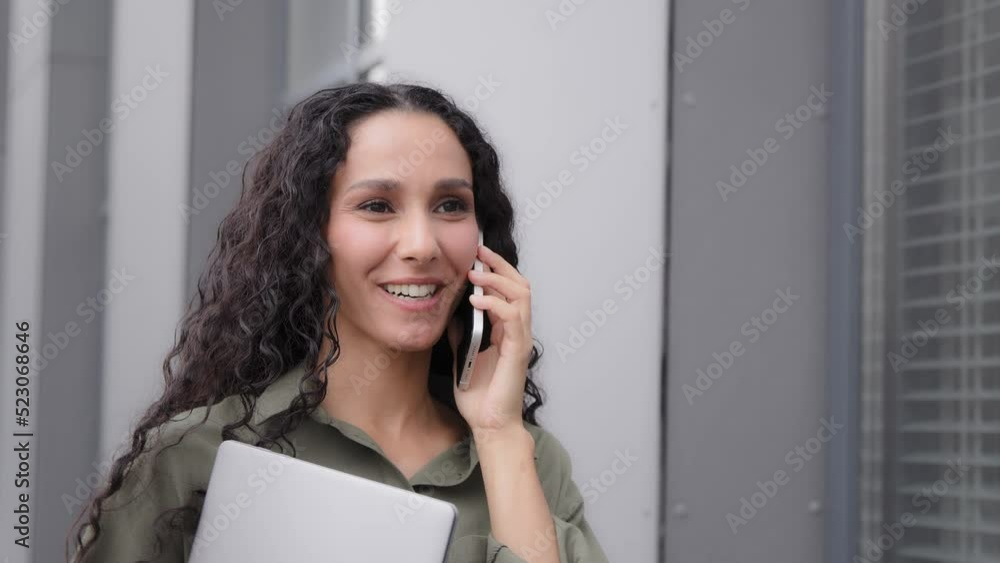 Closeup positive moving business woman 30s ceo manager boss female lady with laptop friendly distant conversation with mobile phone talking smartphone walking on street in city near office building Closeup positive moving business woman 30s ceo manager boss female lady with laptop friendly distant conversation with mobile phone talking smartphone walking on street in city near office building