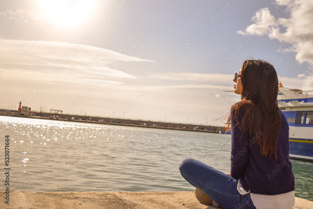 Chica joven sentada mirando el mar en un puerto pesquero 