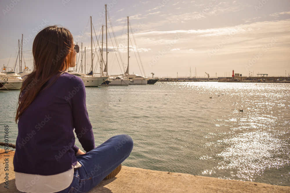 Chica joven sentada mirando el mar en un puerto pesquero 