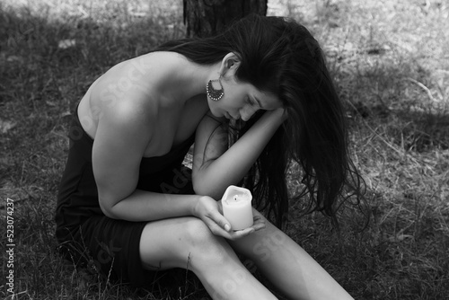 Beautiful woman holding a candle and sitting on the grass in black and white