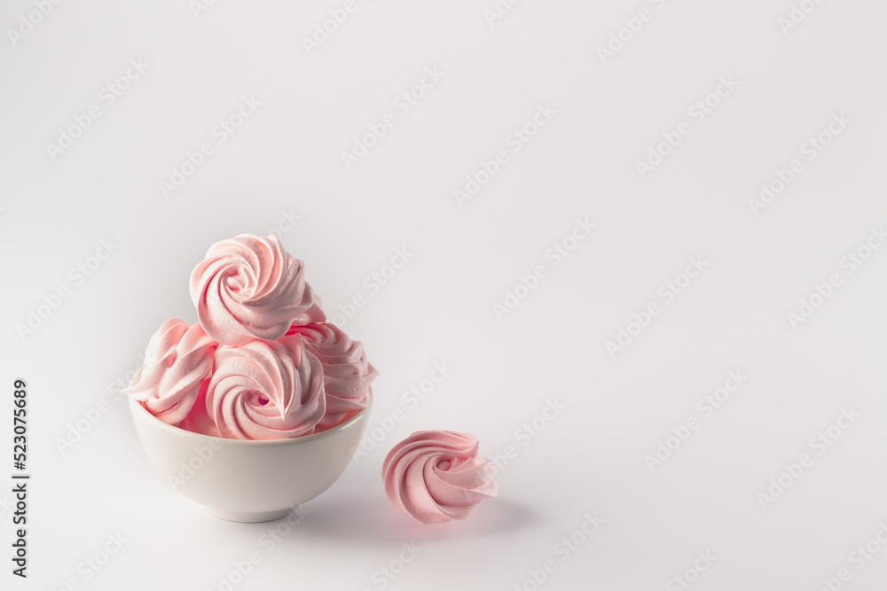 Pink fluffy meringues in a white bowl. Soft soufflé, pastel color. Pink marshmallows in a plate on a white background. Pink fluffy meringues in a white bowl. Soft soufflé, pastel color. Pink marshmallows in a plate on a white background.