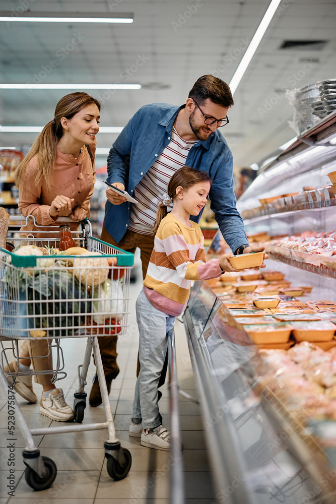 Happy parents and their daughter choosing food at refrigerated section in supermarket.