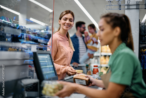 Foto Happy woman putting groceries on checkout counter in supermarket.