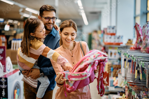 Slika na platnu Little girl and her parents choosing backpack for school while shopping in store together
