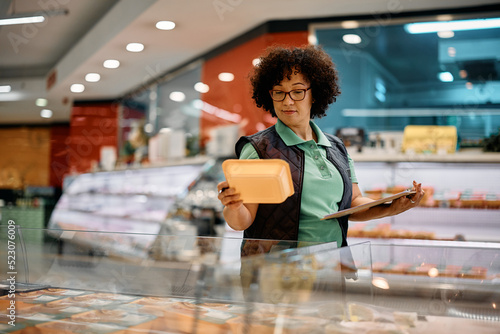 Slika na platnu Female worker checks products in freezer while working in supermarket